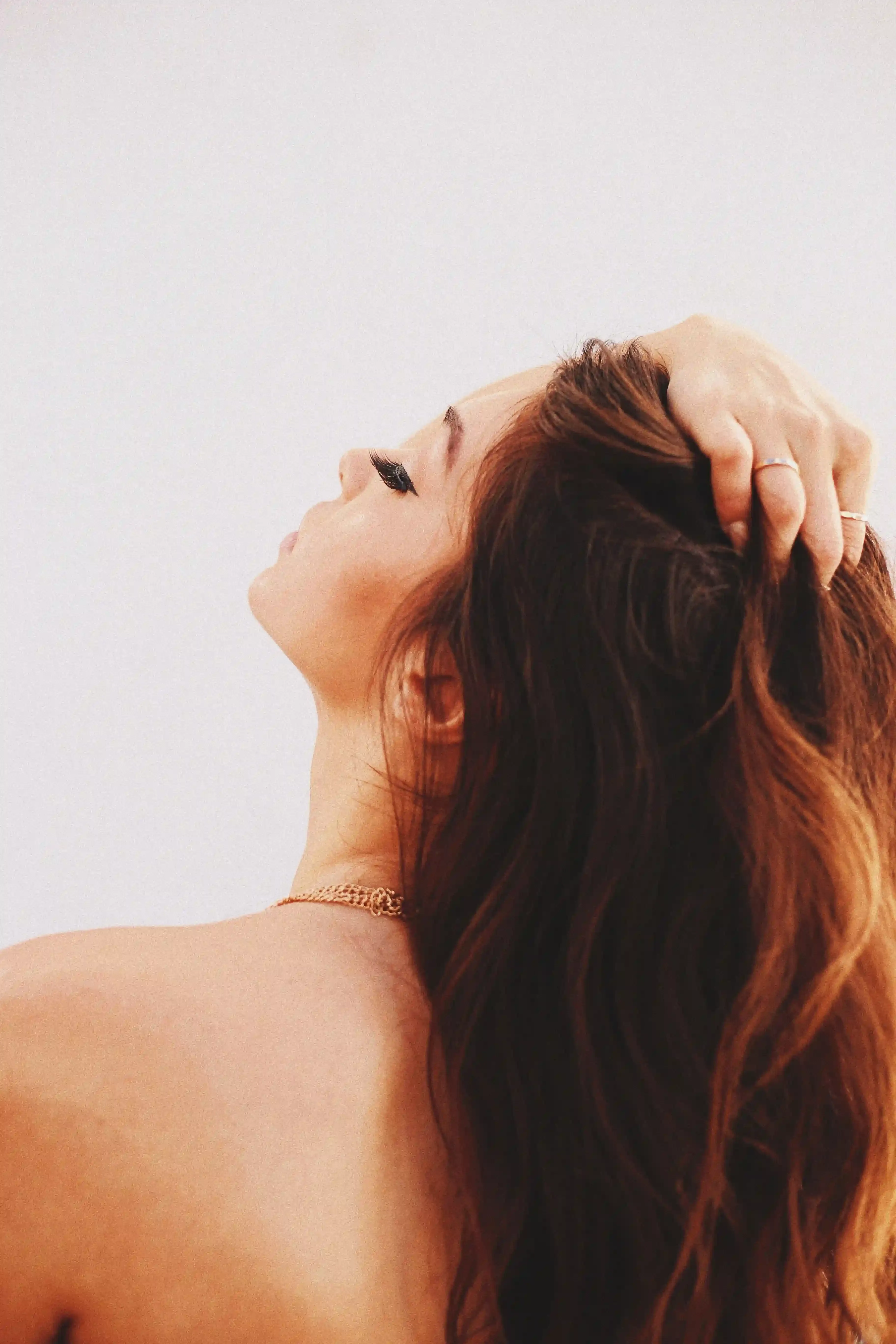 

A woman with long, shiny, and silky hair, wearing a white towel around her shoulders, applying a homemade hair mask to her hair.